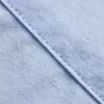 Close-up of the light blue cotton poplin cloth showing the fine plain weave, individual warp and weft threads and a felled seam