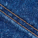 Close-up of the indigo denim twill of the men's denim pants, diagonal weave with white weft flecks through the warp and a double-needle topstitch seam