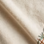 Close-up of the warm cream cotton single jersey knit of the fashion design t-shirts, showing the stitch loops, yarn fibres, a soft fold and the edge of the embroidery