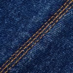 Close-up of the mid indigo denim twill of the jeans pants, diagonal weave ribs with white weft flecks through the indigo warp and a double-needle topstitch seam