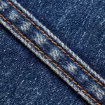 Close-up of the indigo denim diagonal twill weave with indigo warp over white weft, natural slubs and a felled seam with copper double stitching