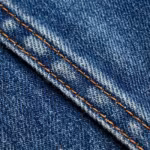 Close-up of the lightweight indigo denim diagonal twill weave with indigo warp over white weft and a felled seam with copper double stitching
