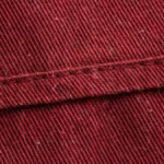 Close-up of the wine red poly-cotton twill weave of the medical scrubs, showing the diagonal rib, individual yarns, natural fibres and a felled seam