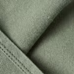 Close-up of the sage green poly-cotton twill weave of the medical unisex scrubs, showing the diagonal rib, individual yarns, natural fibres and a stitched fold