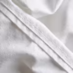 Close-up of the white poly-cotton poplin weave of the medical workwear lab coats, showing individual yarns, natural fibres, soft folds and a felled seam with two stitching rows