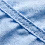 Close-up of the light blue poly-cotton poplin weave of the patient gowns, showing individual yarns, natural fibres, soft folds and a felled seam with two stitching rows
