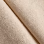 Close-up of the stone beige cotton poplin of the smocked waistband pants, showing the plain weave yarn structure and fibre fly across a soft fold