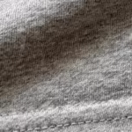 Close-up of the grey marl cotton single jersey knit of the classic t-shirts, showing the stitch loops, heathered yarn fibres, a soft fold and a twin-needle hem row