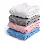 Folded stack of knit undergarments at a three-quarter angle in white, grey marl, soft pink and sky blue - a folded cotton rib vest over folded briefs and a trunk, the folded layers, plain elastic edges and rib knit showing