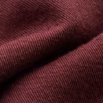 Close-up of the burgundy poly-cotton twill weave of the staff uniforms, showing the diagonal rib, individual yarns and natural fibre hairs across a soft fold