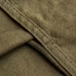 Close-up of the olive heavy cotton canvas weave of the hunting trousers, showing the tight plain weave, yarn structure and the felled panel seam with double-needle stitching