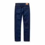 Men's jeans pants in mid indigo denim, back view with yoke seam, two arc-stitched patch back pockets and a plain tan leather patch on the waistband