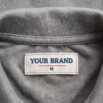Close-up of the inside back neck of the knit cardigan showing the cream woven YOUR BRAND label with navy lettering, a red rule line and the size M mark, stitched into the neck binding