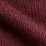 Close-up of burgundy knitted pullover fabric with stocking-stitch loops, matte yarn and fine fibre hairs across a soft diagonal fold