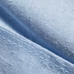 Close-up of the ceil blue poly-cotton poplin weave of the ladies cross over scrub top, showing individual yarns, natural cotton fibres and a felled seam