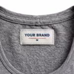 Close-up of the inside back neck of the grey marl ladies vest top showing the cream woven YOUR BRAND label with navy lettering, a red rule line and the size M mark, stitched into the inside back neck below the self-fabric neck binding on the reverse side of the grey marl cotton single jersey