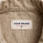 Close-up of the inside back neck of the canvas jacket showing the cream woven YOUR BRAND label with its red rule line and size mark above the shoulder yoke stitching