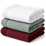 Folded stack of men's cotton briefs in white, sage green and burgundy at a three-quarter angle on white, every piece a classic brief with soft elastic waistbands and elastic-bound leg edges along the folds