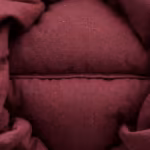Close-up of the burgundy padded jacket cloth, two quilted channels of padding with the channel stitch line between them and the woven yarn structure of the matte shell