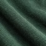 Close-up of forest green cotton pique knit showing the raised pique cells, yarns and fine fibres of the classic polo fabric