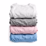 Folded stack of knit undergarments in white, grey marl, soft pink and sky blue - a folded cotton rib vest over folded briefs and a trunk, showing the matte jersey and rib knit of the whole program