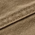 Close-up of the khaki cotton twill weave of the work vest, showing the diagonal rib, yarn structure and fibre fly across a felled seam with double stitching